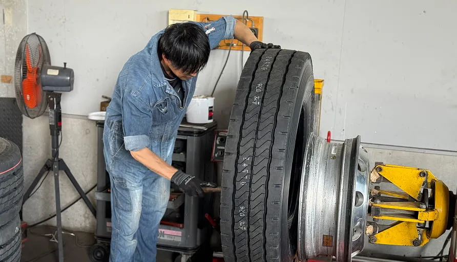 トラック用タイヤを整備機で取り付ける作業員の様子